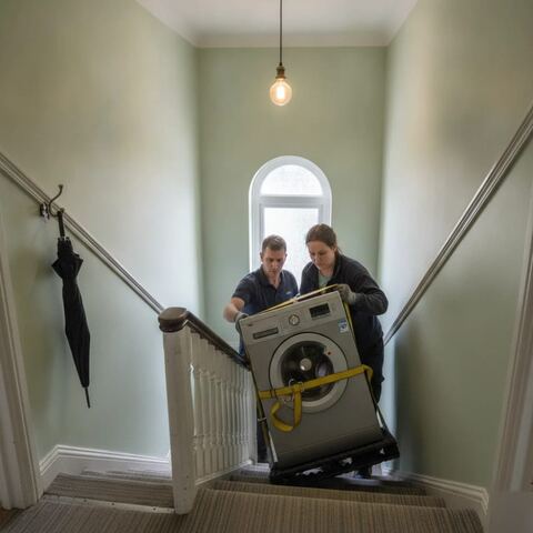 Workers moving washing machine down narrow stairs for appliance disposal Tunbridge Wells